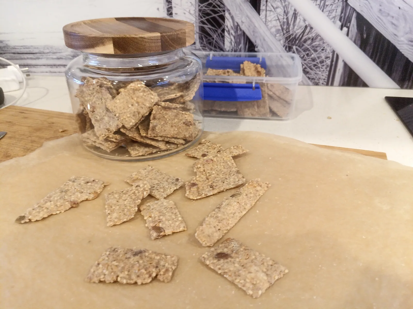 Sourdough discard crackers: baked crackers spread on parchment beside a glass jar of crackers with a wooden lid
