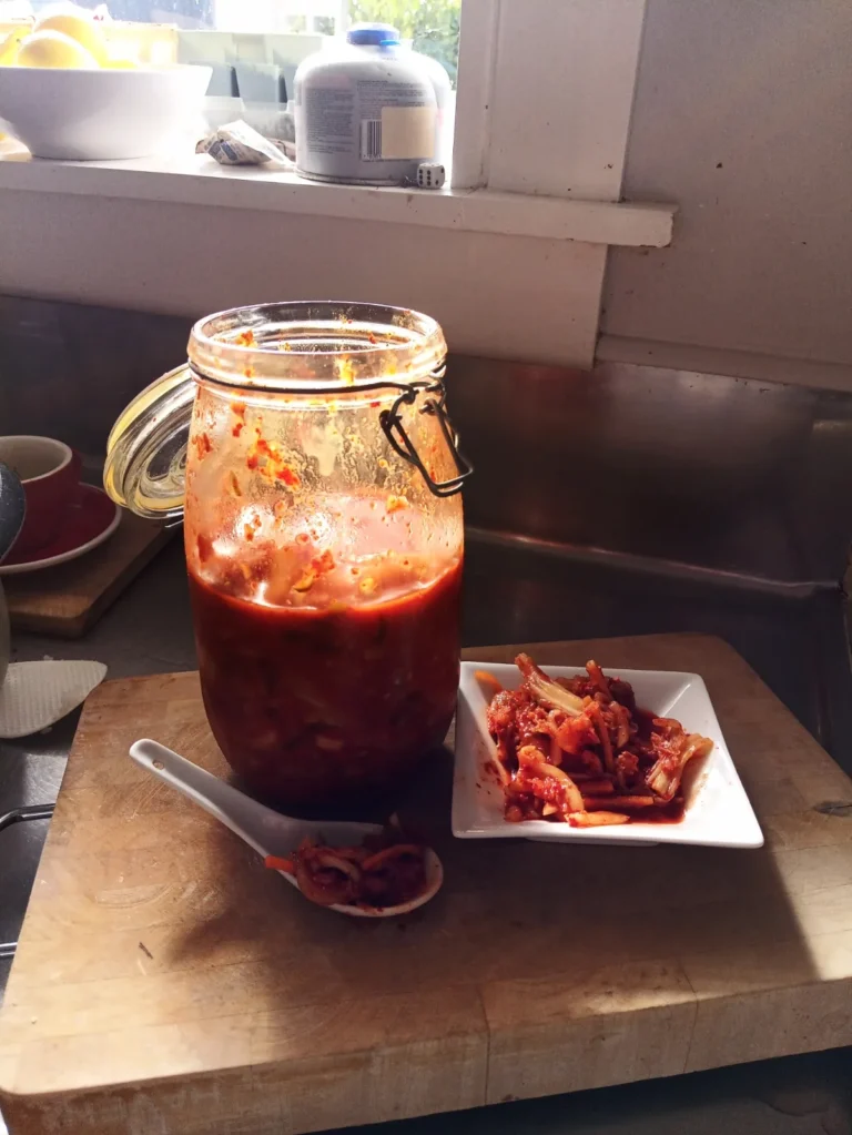 How to make small-batch kimchi: finished kimchi in a hinged glass jar with a spoon and a small plate of kimchi on a wooden board