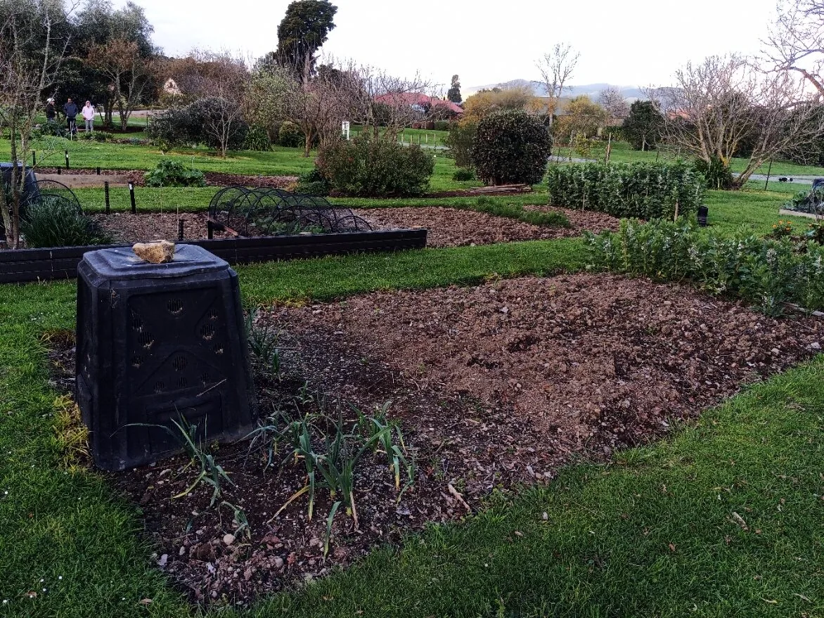 Community garden plots: a shared community garden with a compost bin beside a freshly dug plot and wood-edged beds