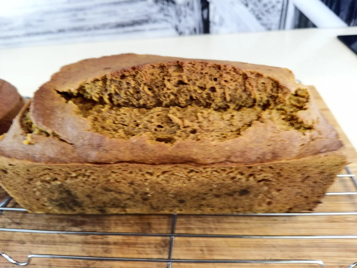 A baked pumpkin loaf on a cooling rack with a well-risen, cracked top and a moist, open crumb.